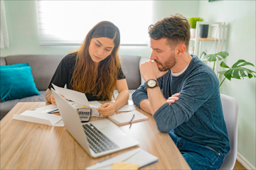 A photo of a young couple sitting at their kitchen table planning for their future.